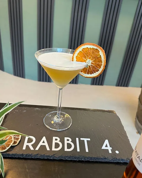 Cocktail im Coupé-Glas mit getrockneter Orangenscheibe auf einer Schieferplatte mit dem Schriftzug Rabbit 4