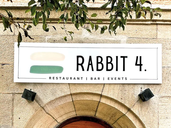 Weißes Schild mit dem Schriftzug Rabbit 4 und dem Zusatz Restaurant Bar Events über dem Eingangsbogen